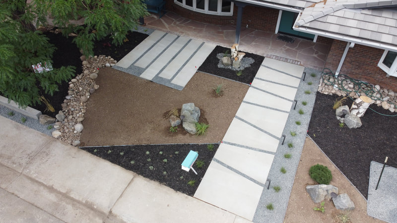 DRONE VIEW OF A CUSTOM LANDSCAPE DESIGNED BY AMY ROOT. The front yard is located in the Rolling Hills subdivision of Golden, CO.  It's a very modern design with concrete slabs both rectangular and angular.  The angular path leads to the front door with a very modern feel of rocks, dark mulch and simple plantings.