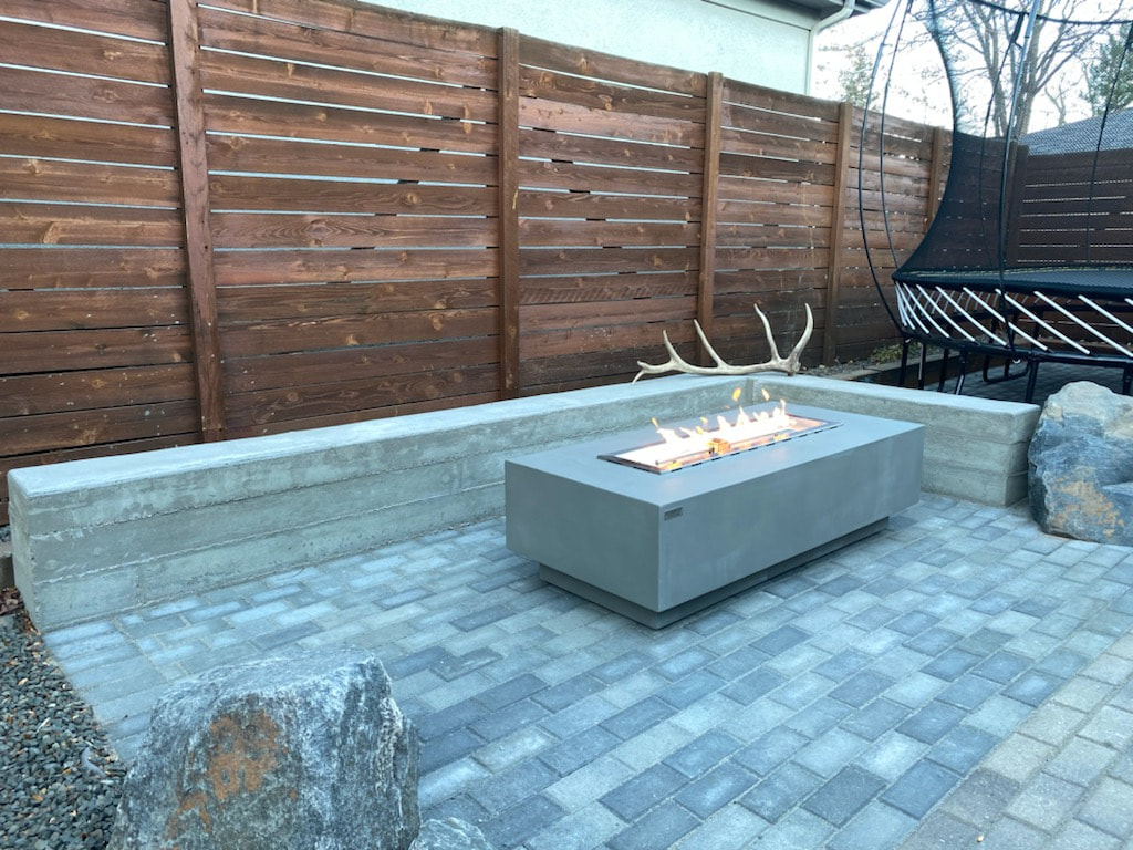 Modern Gas Fire Pit surrounded by a board formed concrete seating wall on paver patio